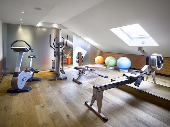 Un gimnasio con equipo de ejercicio, piso de madera y tragaluz.