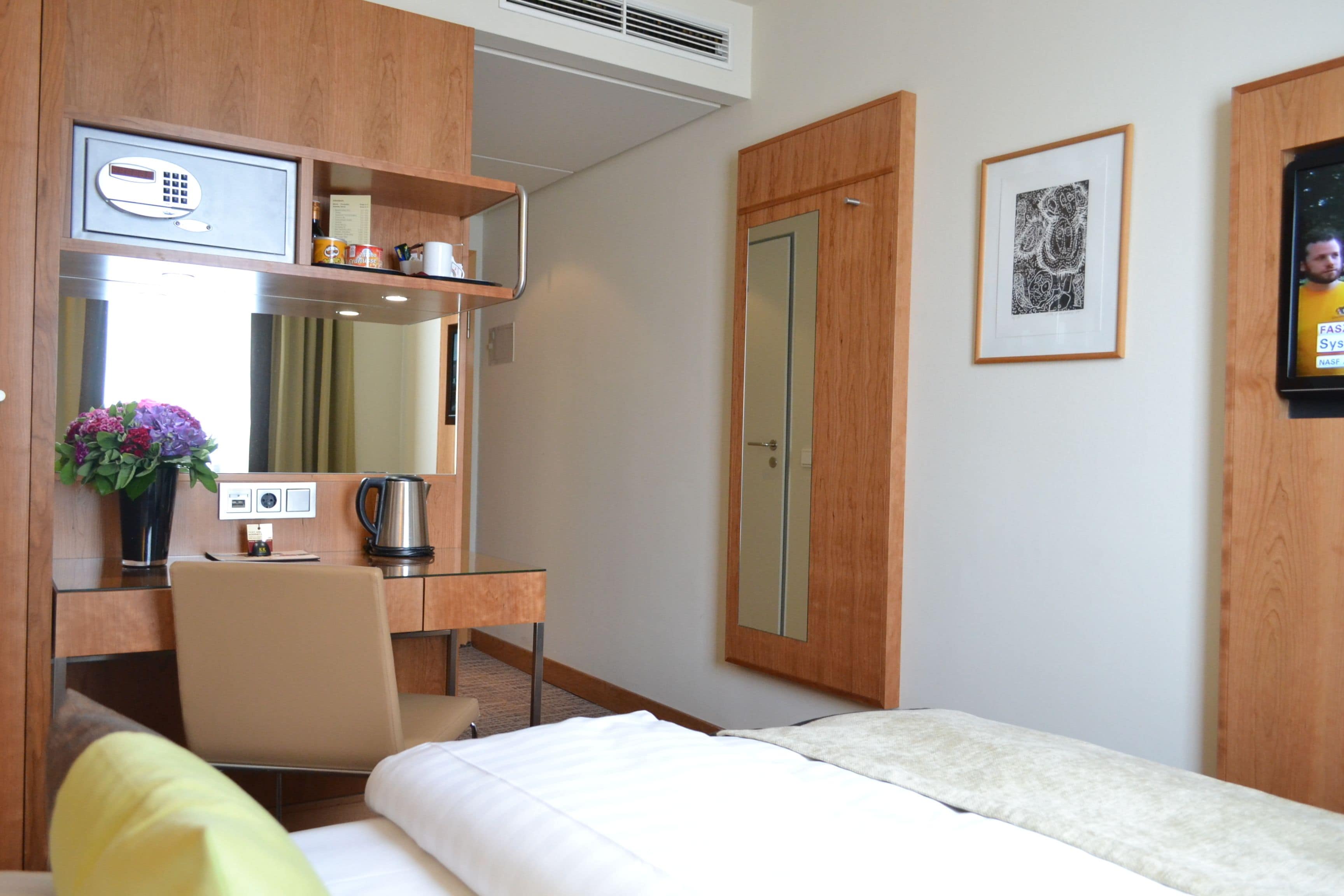 Une chambre d’hôtel avec un lit, un bureau avec un ordinateur, un miroir, une machine à café et un tableau encadré au mur.