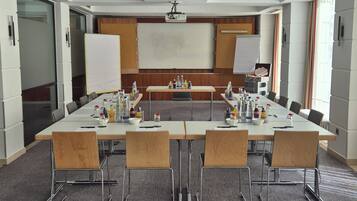 Una sala de conferencias con una mesa larga, sillas, una pantalla de proyector y una pizarra.