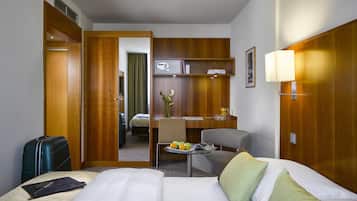 Habitación de hotel con cama, escritorio, silla, pequeña mesa con frutas y una maleta.