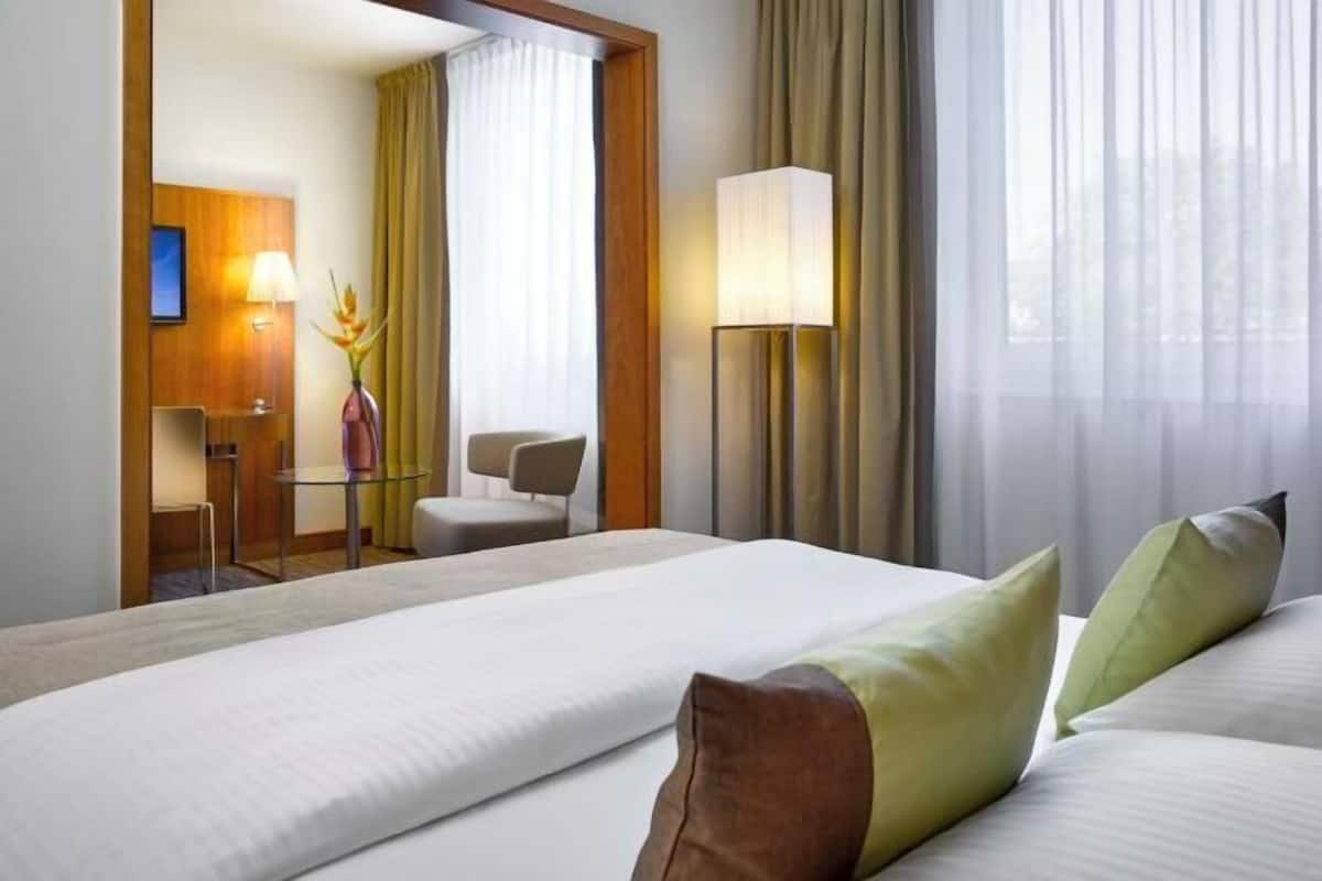 Habitación de hotel con cama, escritorio con silla, lámpara y vistas al exterior.
