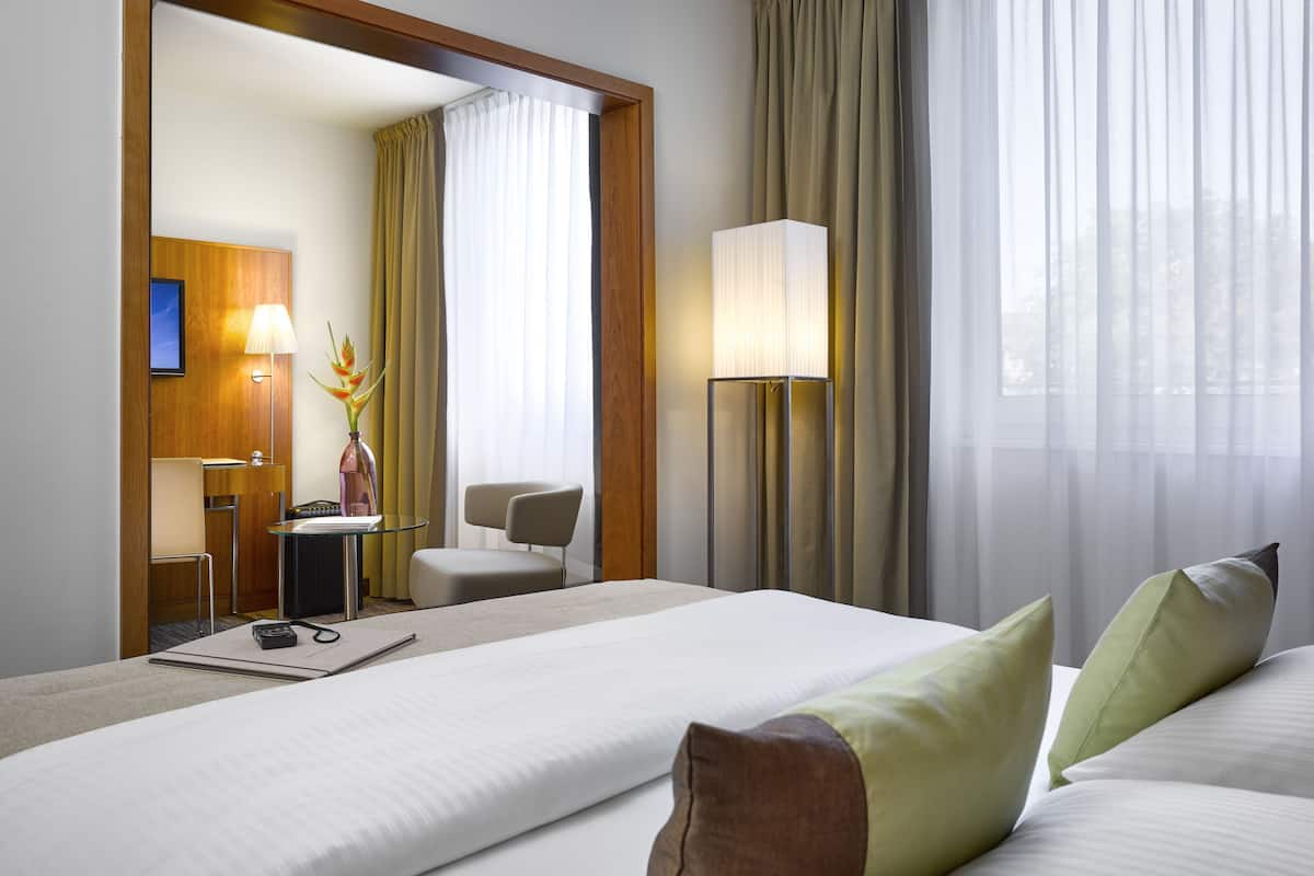 Habitación de hotel con cama, escritorio, silla, lámpara y vistas al exterior.