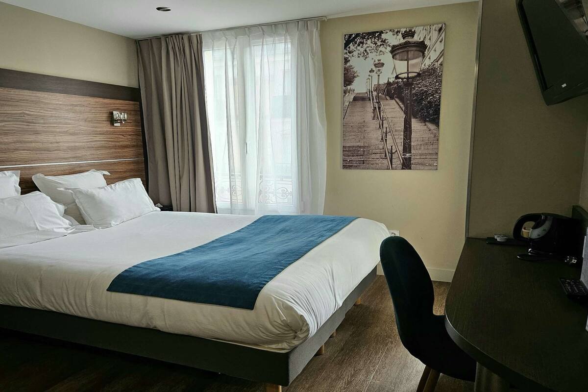 Une chambre d’hôtel équipée d’un lit, d’un bureau, d’une chaise, d’une télévision et d’une fenêtre avec des rideaux.