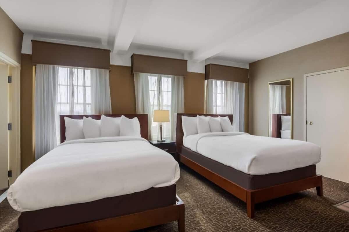A hotel room with two beds, a nightstand, a lamp, and a mirror.