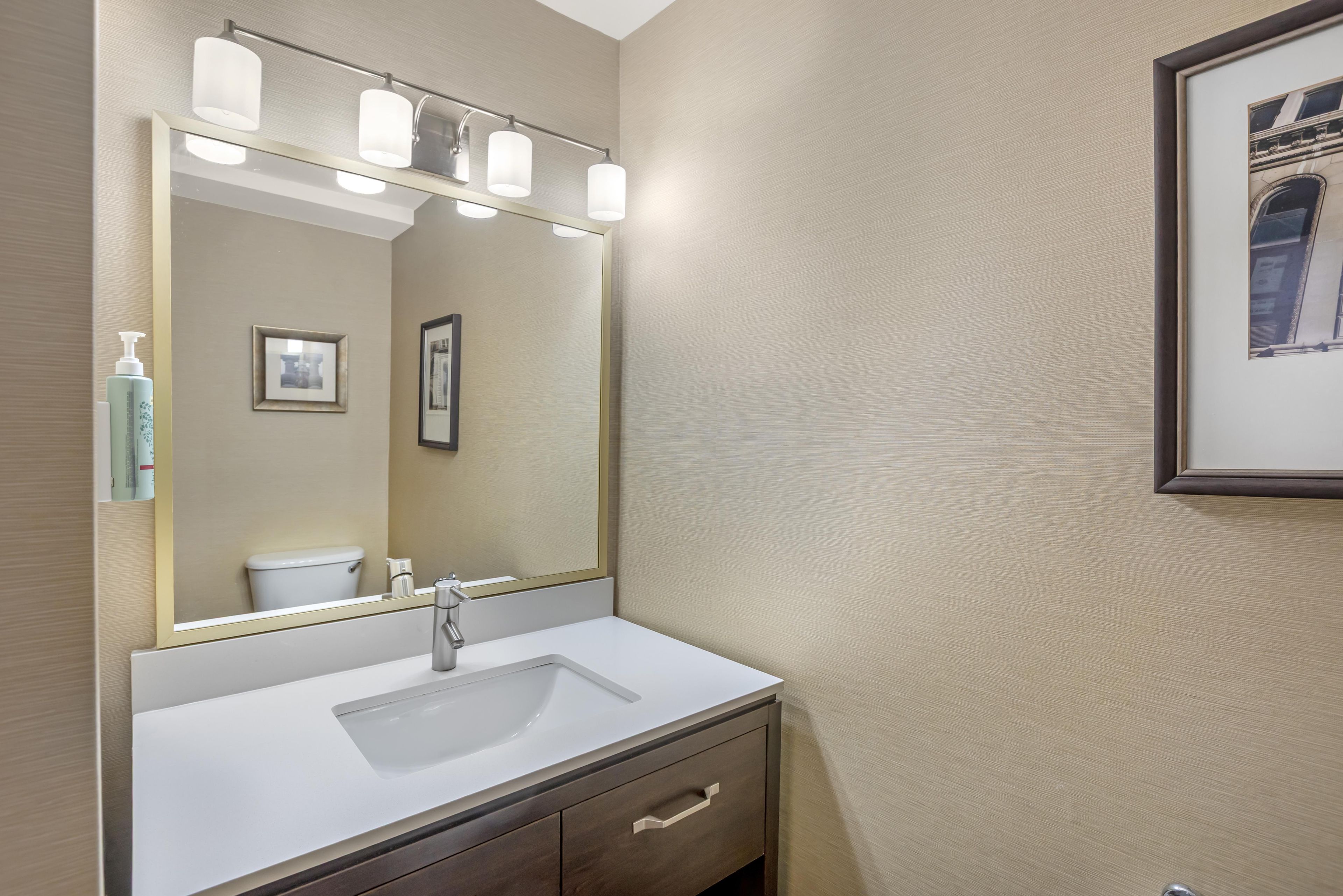 A bathroom with a large mirror, a white sink, a dark wooden cabinet, and a framed picture on the wall.