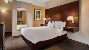 Habitación de hotel con una cama grande, dos mesitas de noche con lámparas, un espejo y un cuadro en la pared.