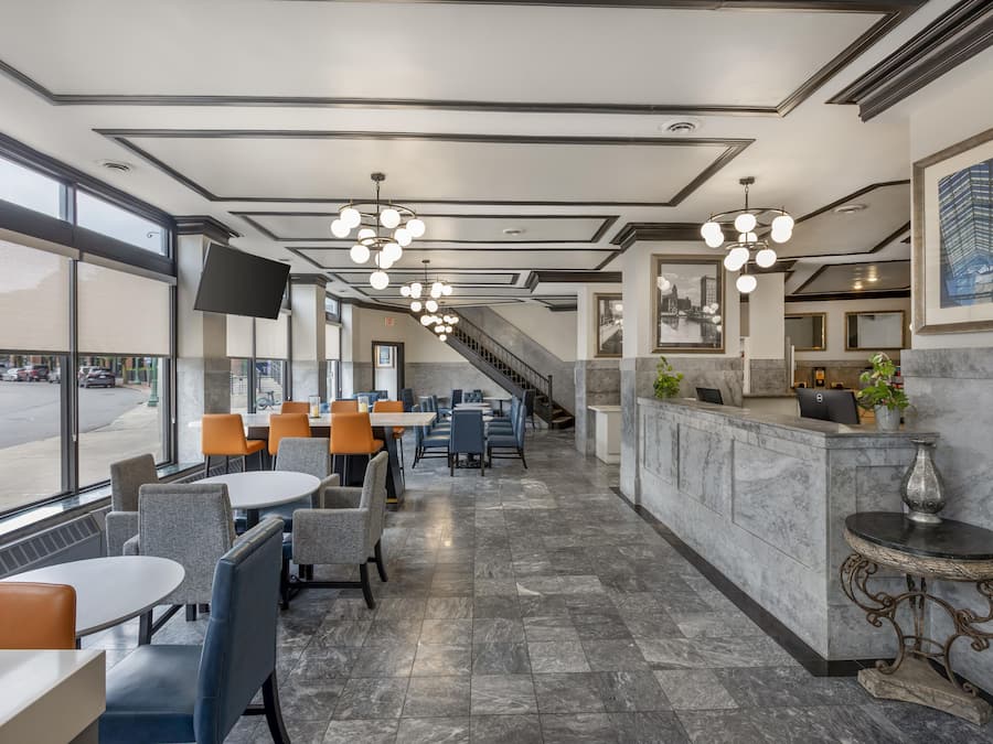 Eine Hotelhalle mit Rezeption, Sitzgelegenheiten und einer Treppe zu den oberen Stockwerken.