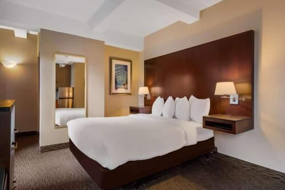 A hotel room with a large bed, bedside lamps, a mirror, and a framed picture on the wall.