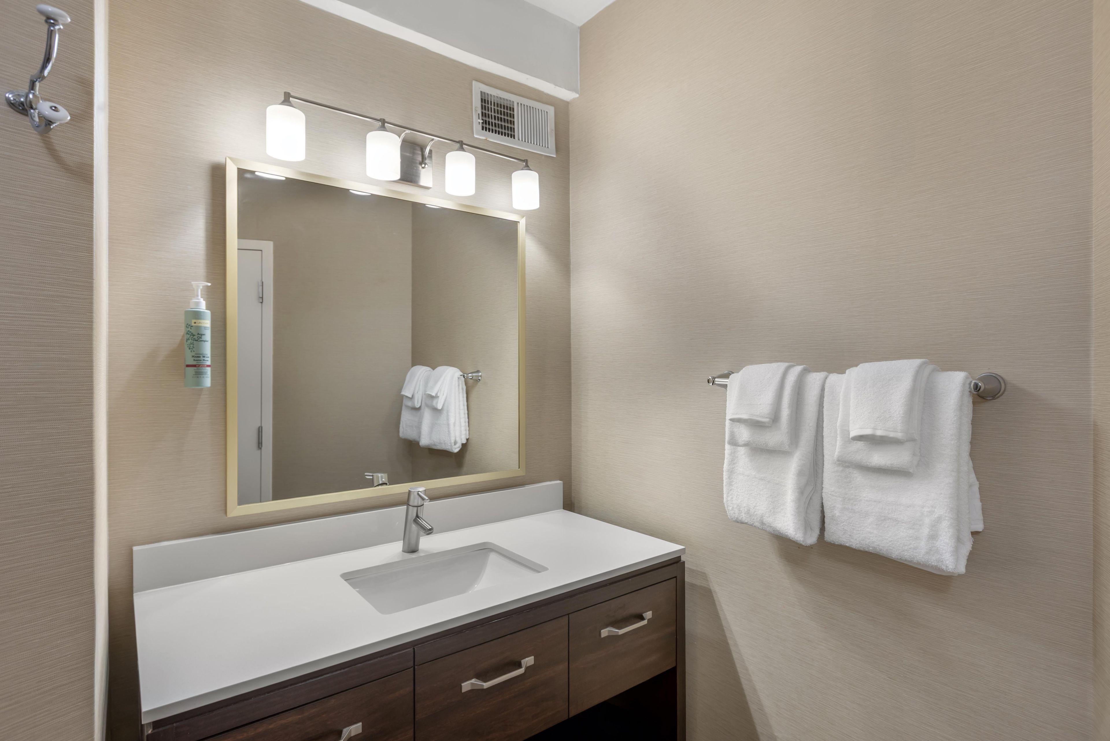 A bathroom with a large mirror, a sink, and a towel rack.