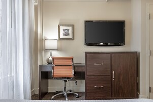 Una habitación de hotel con escritorio, una silla, televisor y armario.