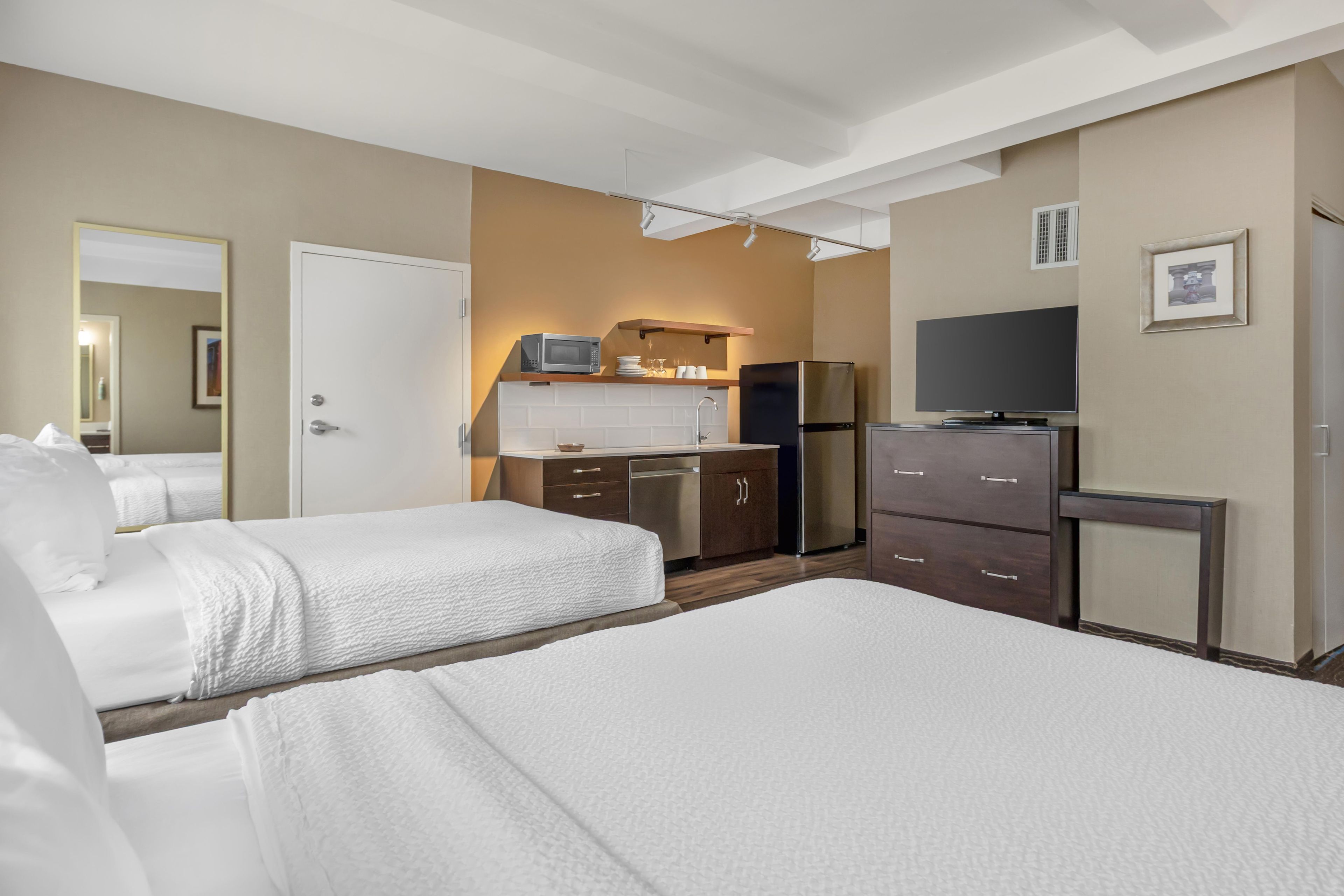 Quarto de hotel com duas camas, cozinha compacta, televisão e banheiro.