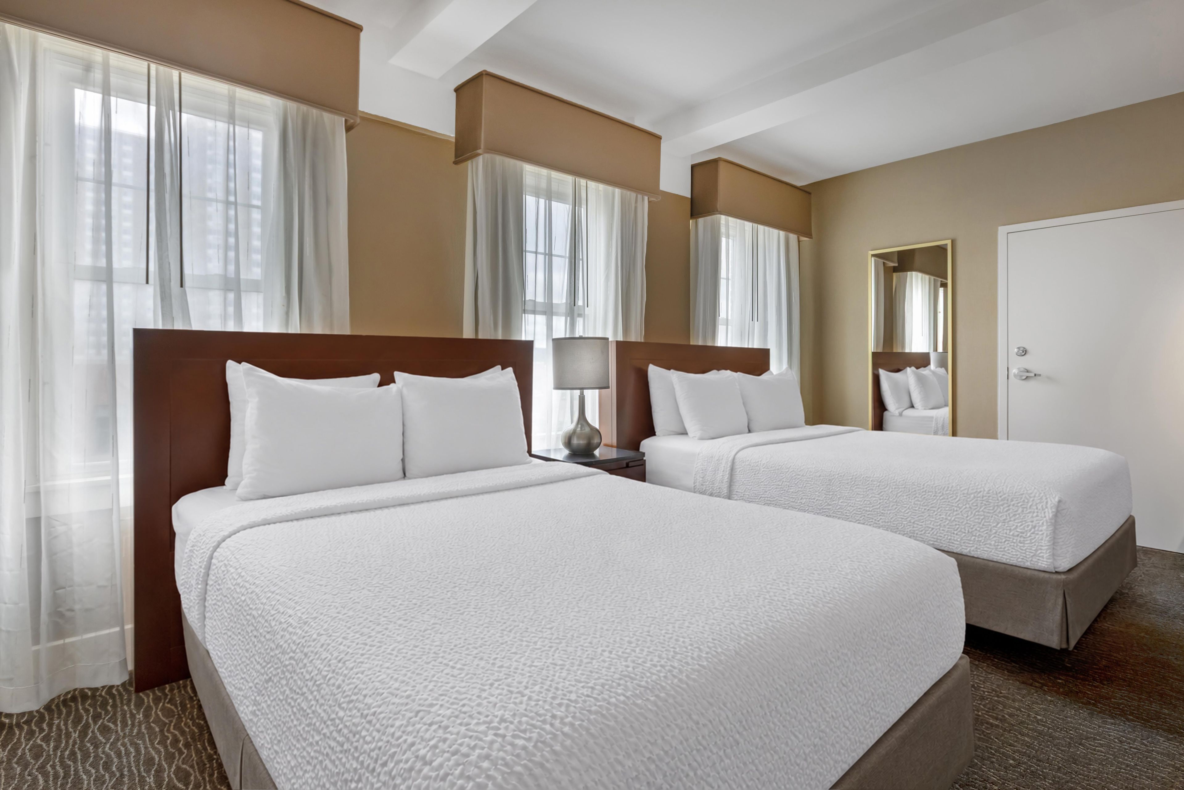 Habitación de hotel con dos camas, una mesita de noche, una lámpara y un espejo.