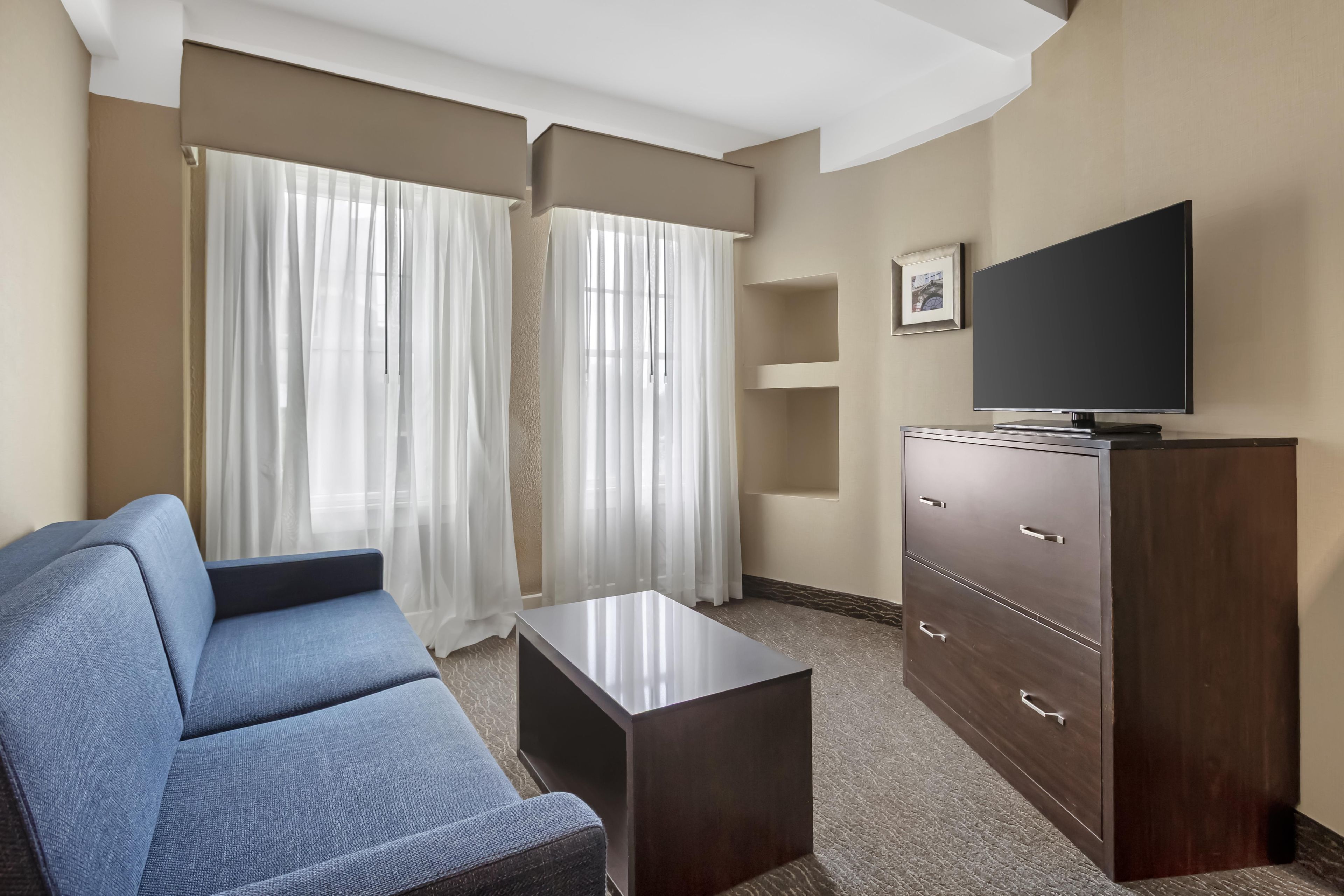 Una habitación de hotel con sofá, televisor en un mueble y ventana con cortinas.