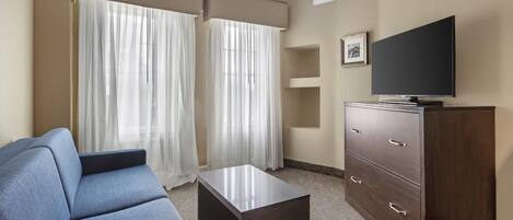 Una habitación de hotel con sofá, televisor en un mueble y ventana con cortinas.