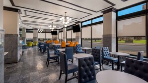 Un restaurante moderno con una barra larga, sillas azules y anaranjadas, y grandes ventanales con vistas a la calle.