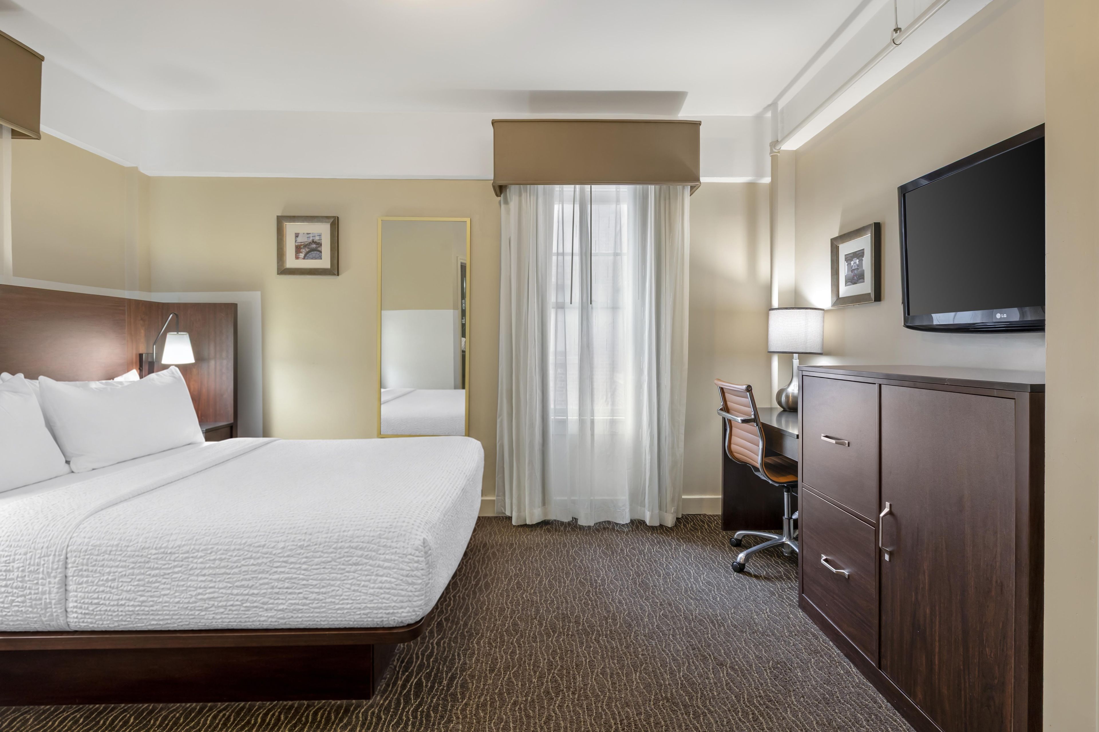 Een hotelkamer met een bed, een bureau met stoel, een televisie en een kledingkast.