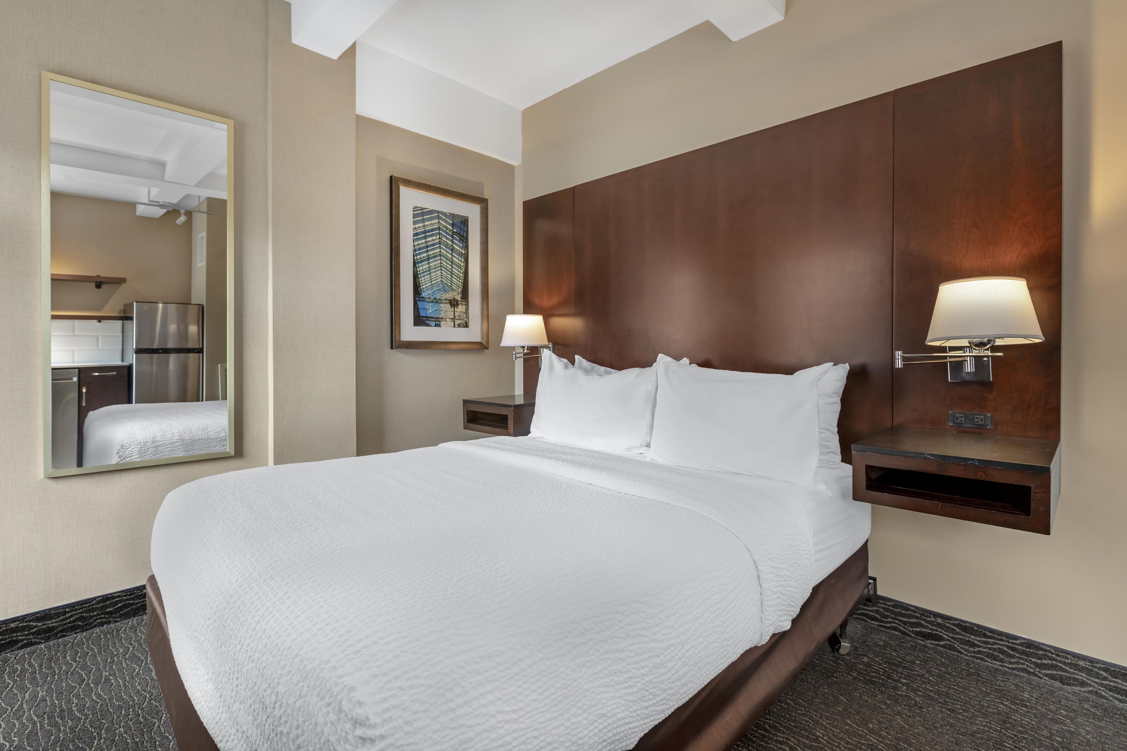 A hotel room with a large bed, a nightstand with a lamp, a mirror, and a framed picture on the wall.