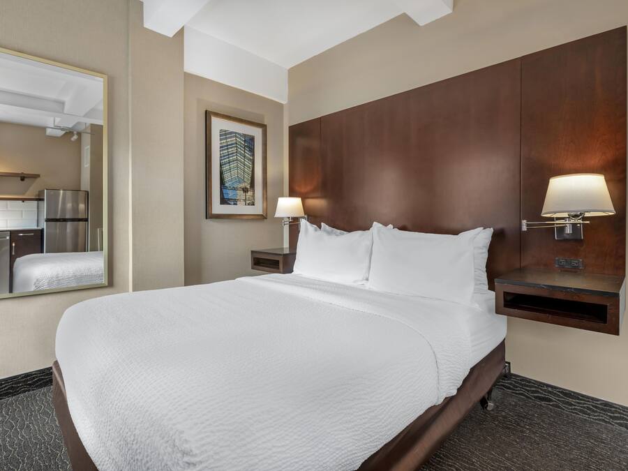 Quarto de hotel com uma cama grande, mesa de cabeceira com abajur, espelho e um quadro na parede.