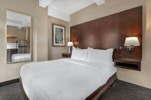 Habitación de hotel con una cama grande, una mesita de noche con lámpara, un espejo y un cuadro en la pared.