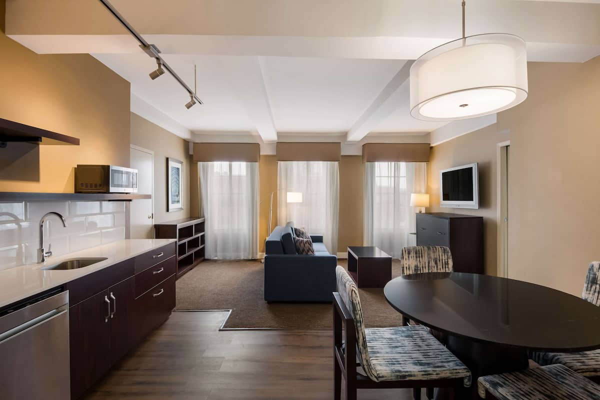 A modern hotel room with a kitchen, dining area, and living space.