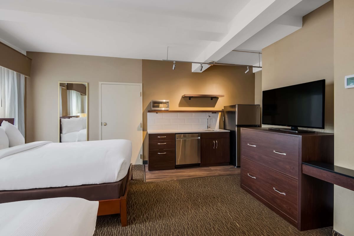 A hotel room with a bed, a television, a microwave, a refrigerator, and a small kitchenette.