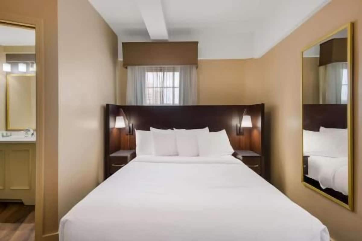 A hotel room with a large bed, two bedside tables with lamps, a mirror, and a window with curtains.