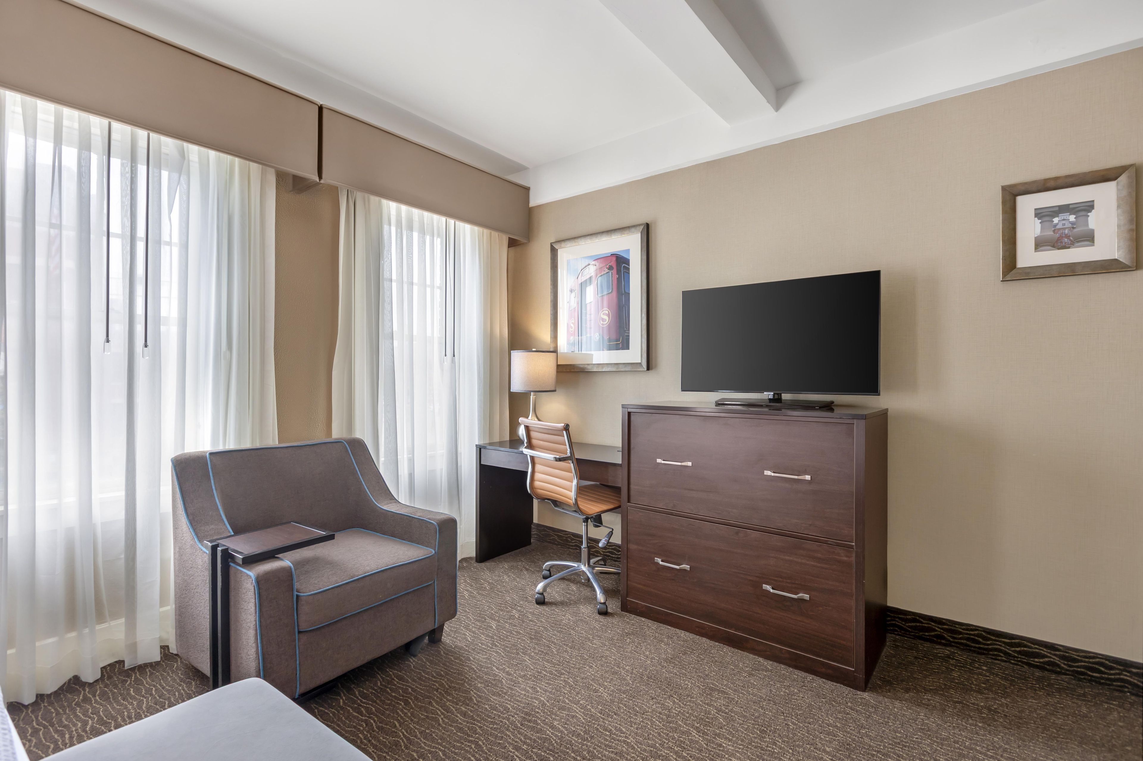 A hotel room with a bed, a desk, a chair, a television, and a dresser.
