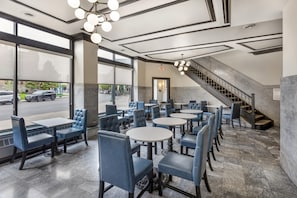 Interior de restaurante con varias áreas de estar, incluyendo mesas y cabinas, una escalera y grandes ventanales que dan a la calle.