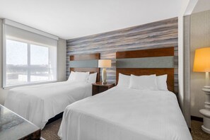Habitación de hotel con dos camas, una mesita de noche con lámpara, una ventana y vistas a la ciudad.