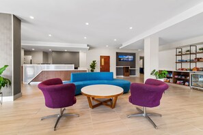Un vestíbulo moderno con una recepción, un sofá azul y sillas moradas alrededor de una mesa redonda.