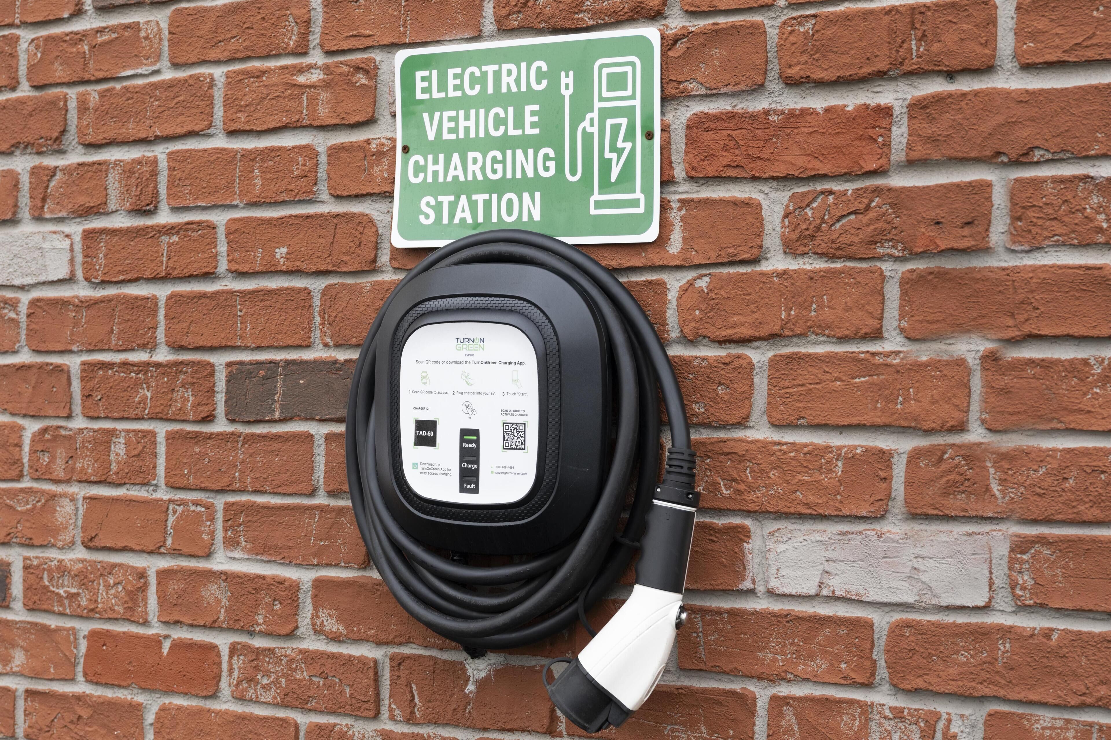 An electric vehicle charging station with a charging cable and a sign indicating its purpose.