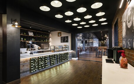 A modern coffee shop interior with a counter, shelves with plants, and a seating area.