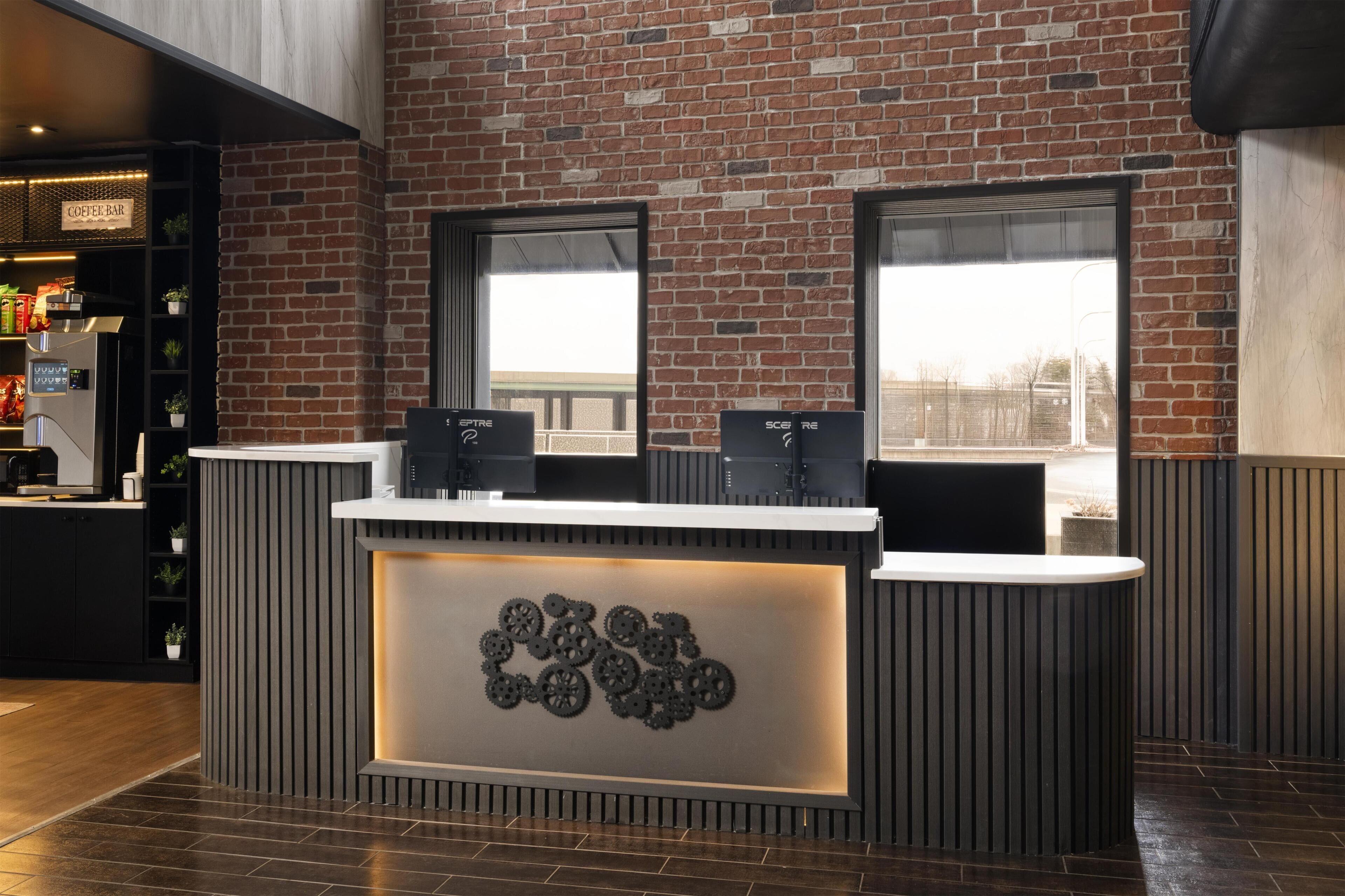 A reception desk with a brick wall backdrop, two large windows, and a modern design with a central decorative element.