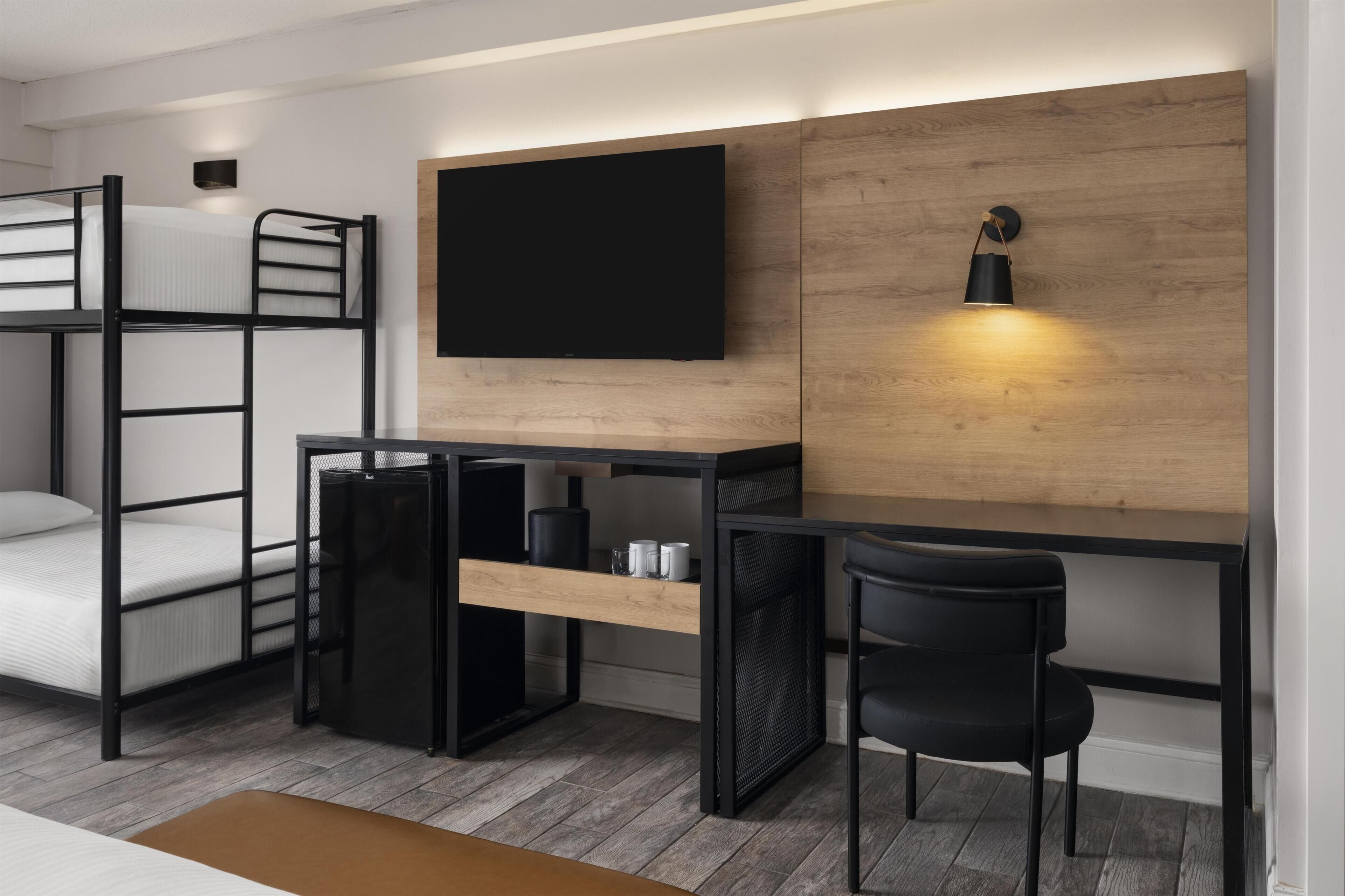 Una cama litera con escritorio y silla, un televisor de pantalla plana y una lámpara de pared.
