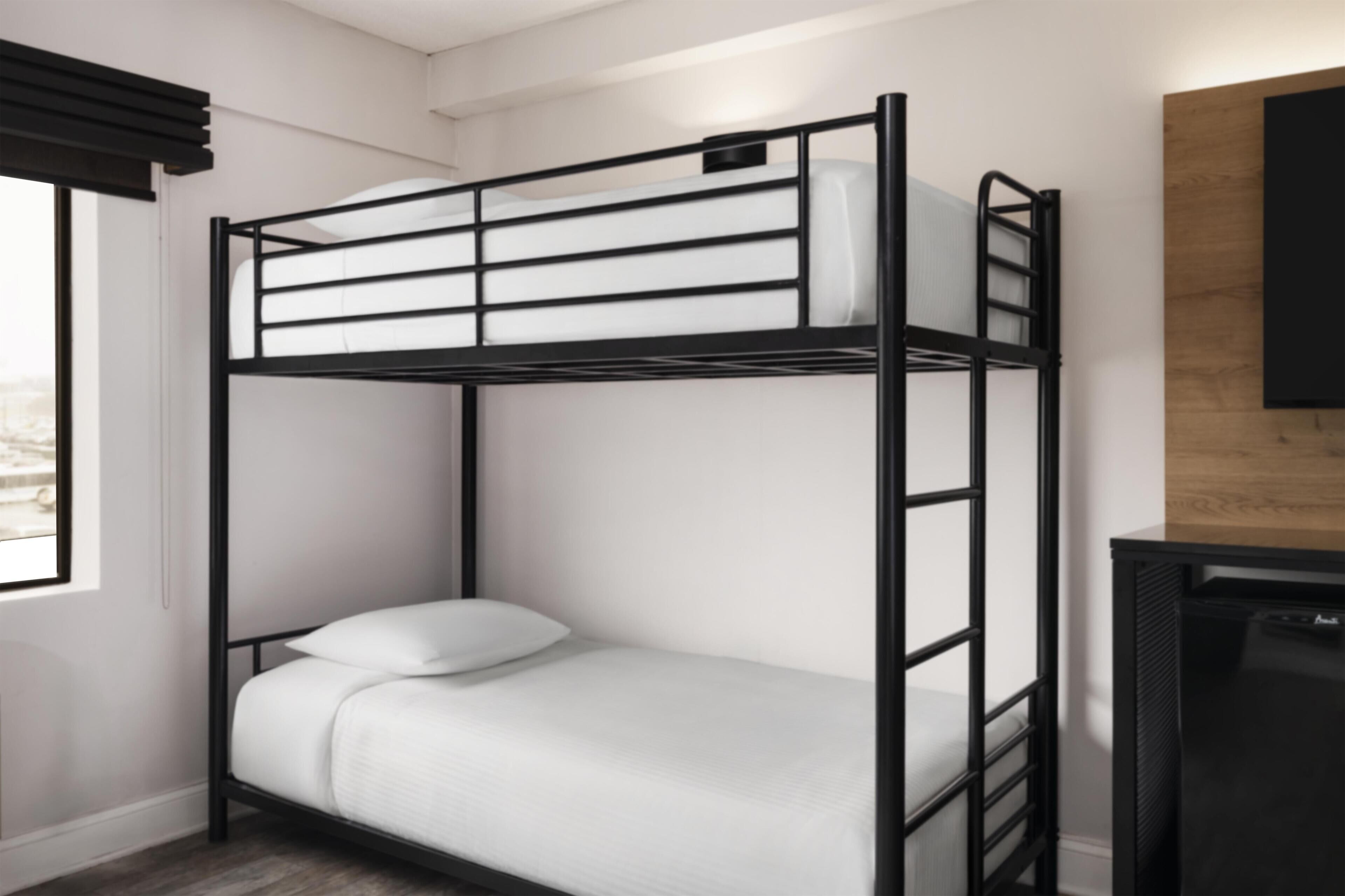 Un lit superposé avec un matelas blanc, une structure en métal noir et un panneau en bois sur le mur.