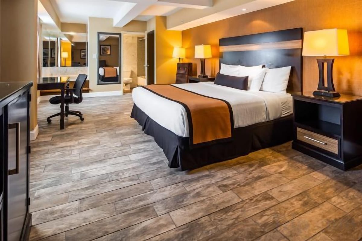 Una habitación de hotel con una cama grande, mesitas de noche con lámparas, un escritorio con una silla y una televisión.