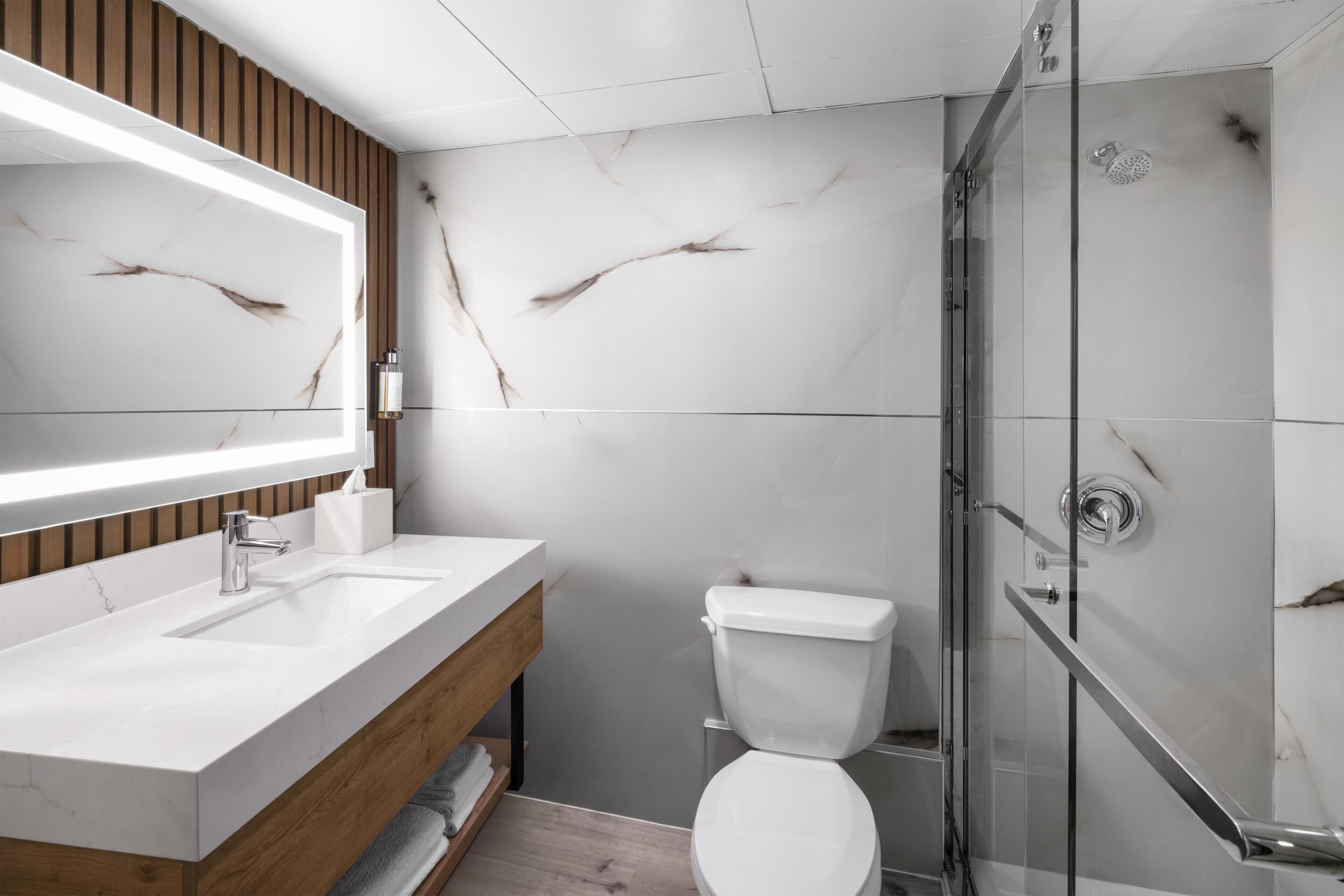 A modern bathroom with a wooden vanity, a glass shower enclosure, and marble walls.