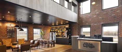 A spacious lobby with a high ceiling, exposed brick walls, a reception desk, and a seating area with leather chairs and tables.