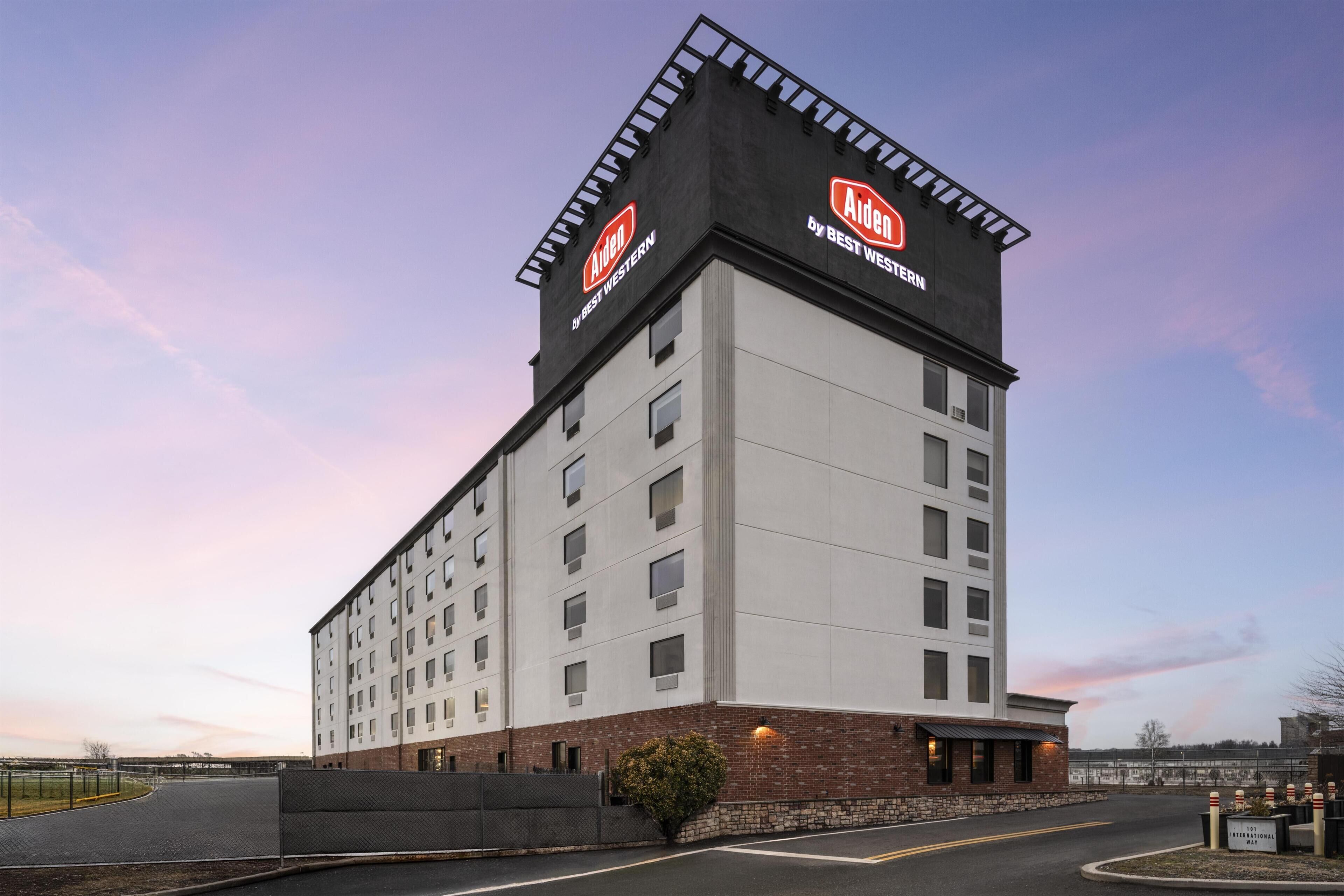 A large hotel building with multiple floors, a prominent Aiden by Best Western sign, and a brick base.