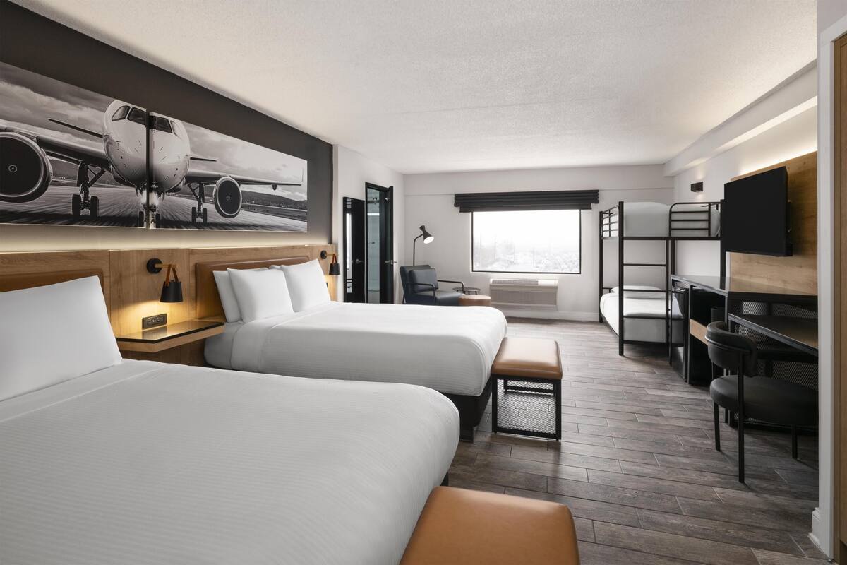 A hotel room with two beds, a desk, a chair, a TV, and a large window.