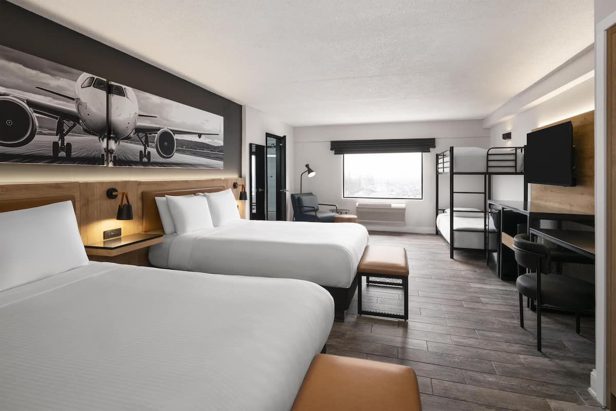 Habitación de hotel con dos camas, un escritorio, una silla, un televisor y un ventanal grande.