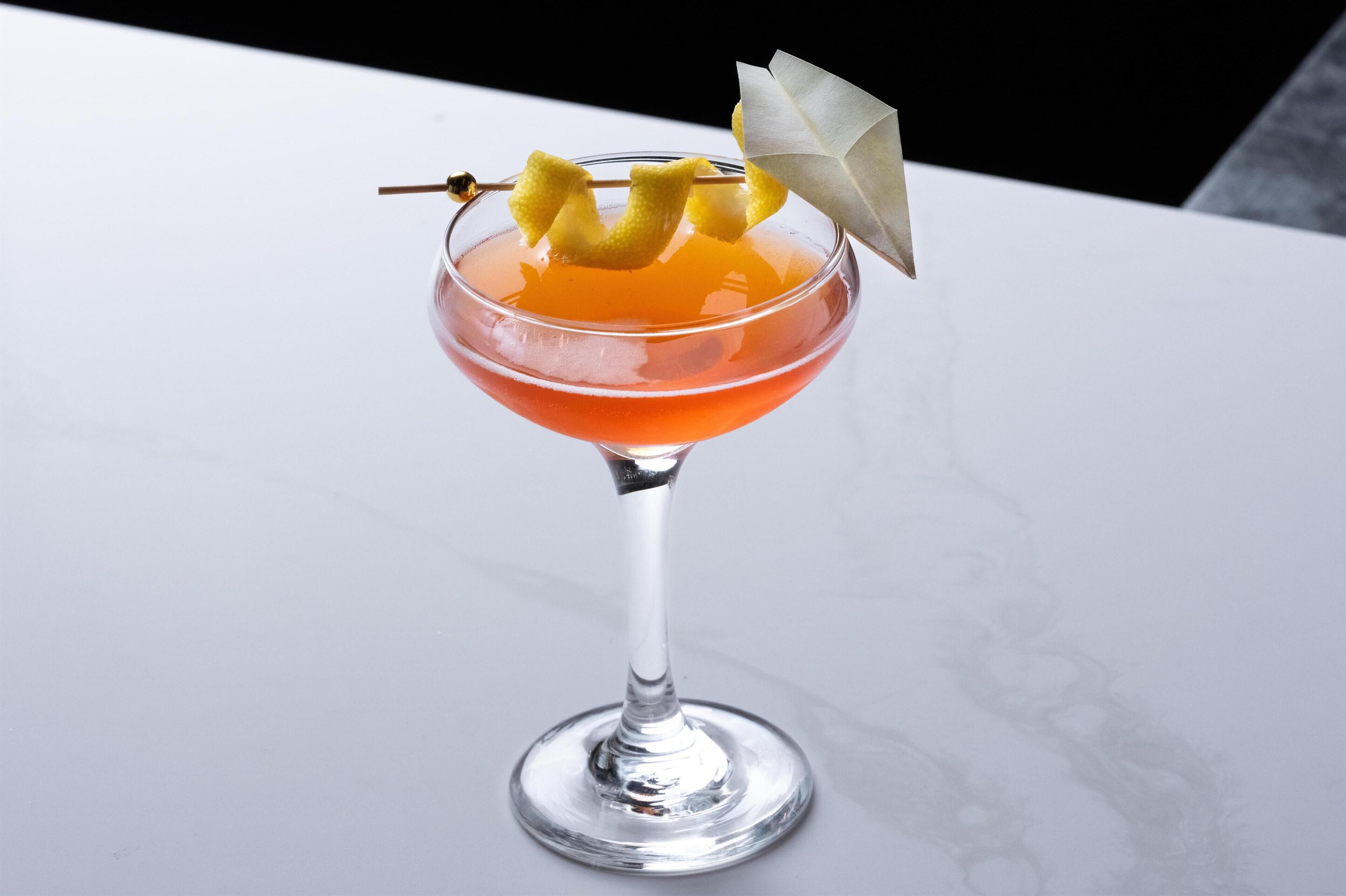 A cocktail in a stemmed glass with a garnish and a folded napkin.