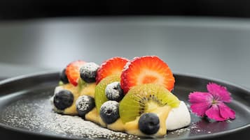 Postre con fresas, arándanos, kiwi y una flor rosa sobre un plato negro.