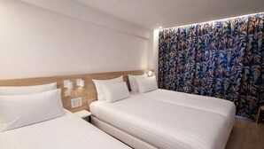 Habitación de hotel con dos camas, cabecero de madera y cortina con estampado floral.