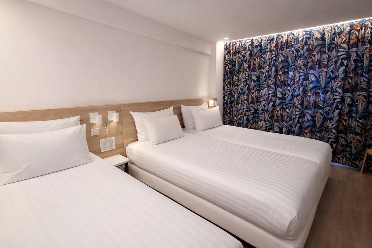 Ein Hotelzimmer mit zwei Betten, einem hölzernen Kopfteil und einem Vorhang mit Blumenmuster.