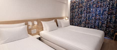 Habitación de hotel con dos camas, cabecero de madera y cortina con estampado floral.