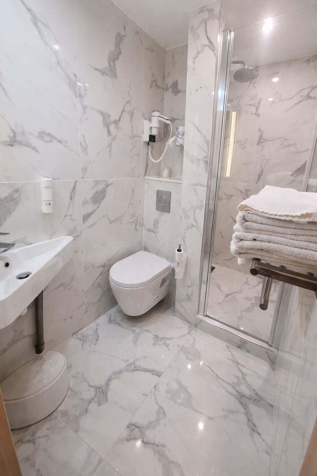 Un bagno moderno con pavimento in marmo, cabina doccia in vetro, un water e un lavandino con portasciugamani.
