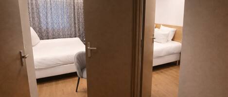 Una habitación de hotel con piso de madera, una cama con ropa blanca, una silla y una puerta.