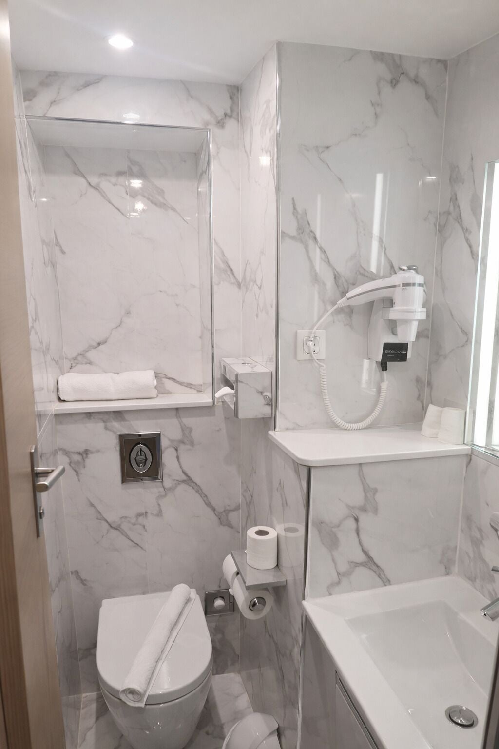 A bathroom with a marble wall, a glass shower enclosure, a toilet, a bidet, and a bathtub.