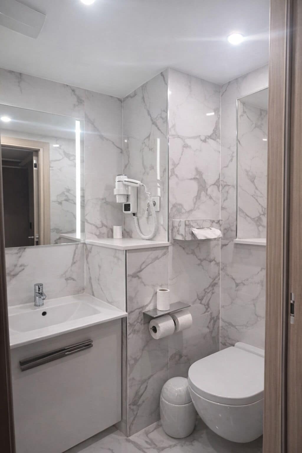 A modern bathroom with a marble backsplash, a sink, a toilet, and a hairdryer on a shelf.